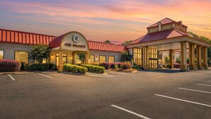 A hotel with a red roof, a central entrance, and a parking lot. - Village Inn Clemmons/Winston Salem, Trademark by Wyndham (Clemmons)