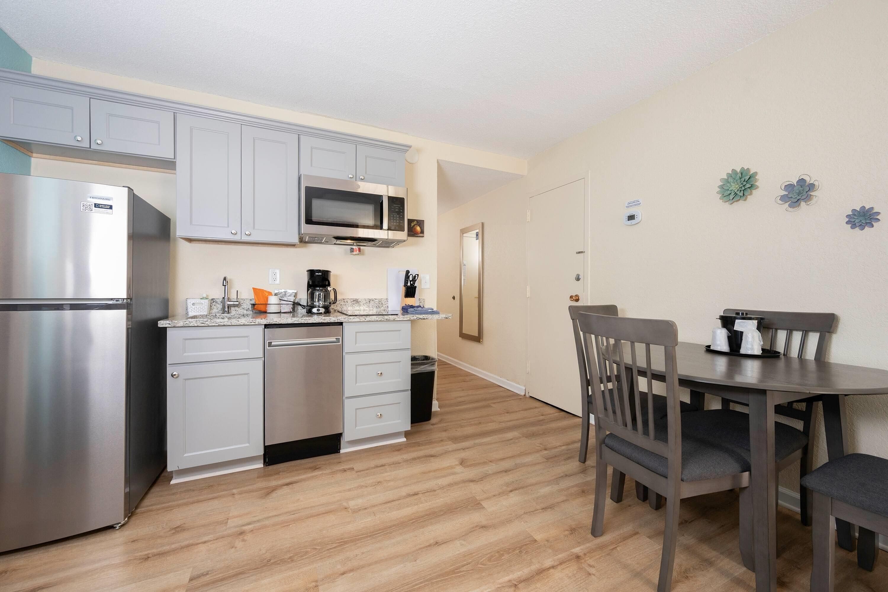 A compact kitchen with a refrigerator, microwave, and coffee maker. There is a dining table with chairs and a trash can.