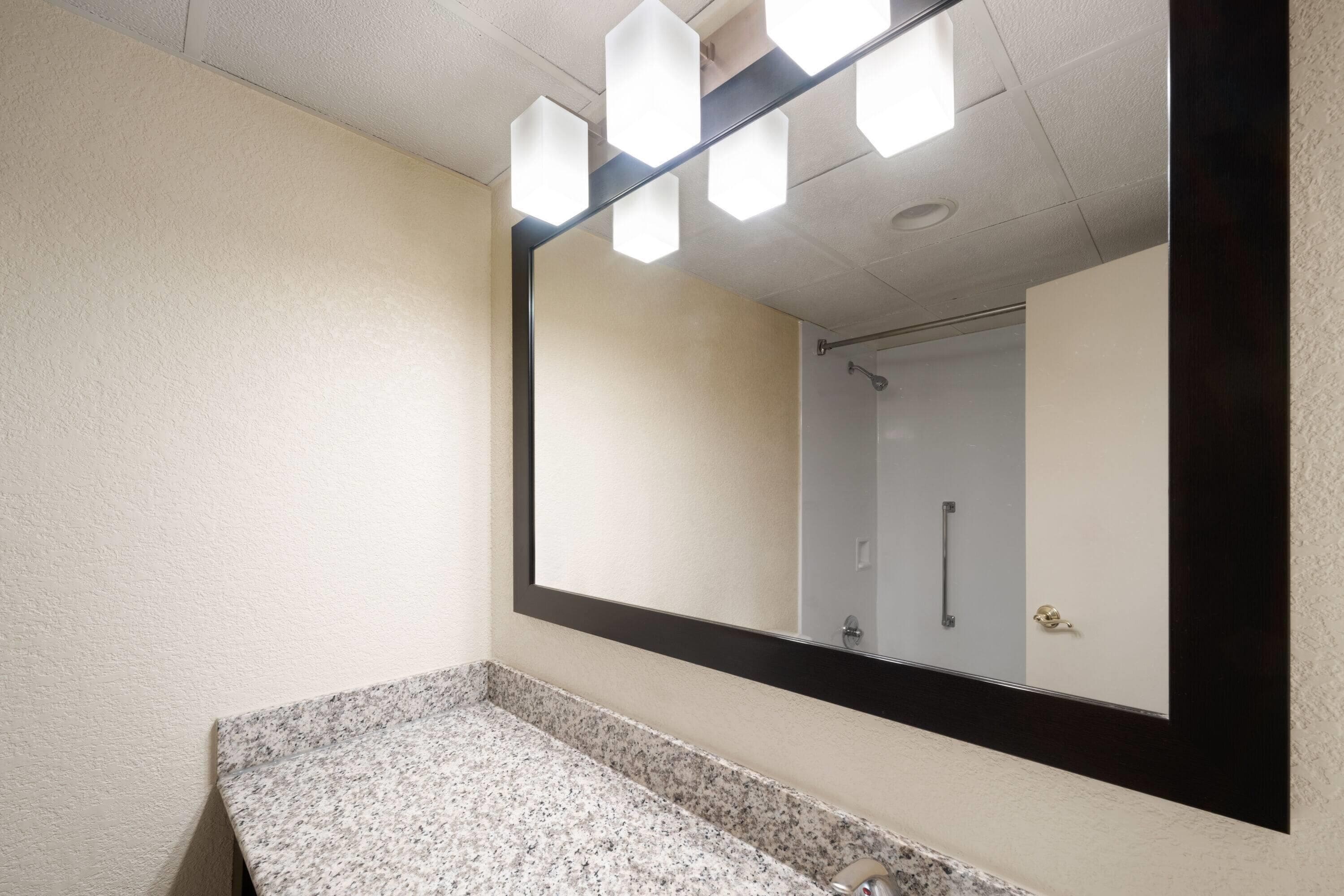 A bathroom with a granite countertop, a large mirror, and a shower visible in the background.