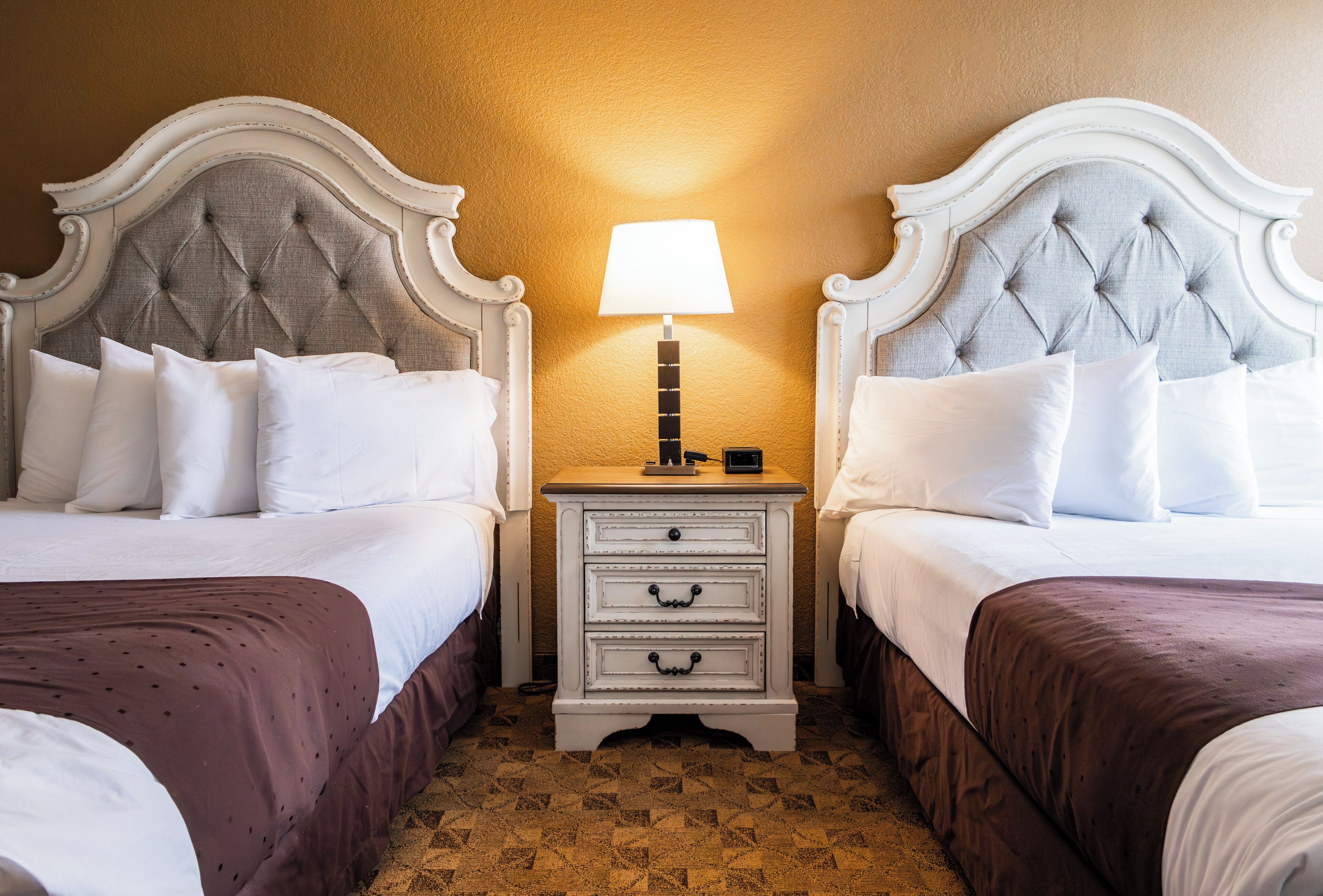 A hotel room with two beds, a nightstand with a lamp, and a patterned carpet.