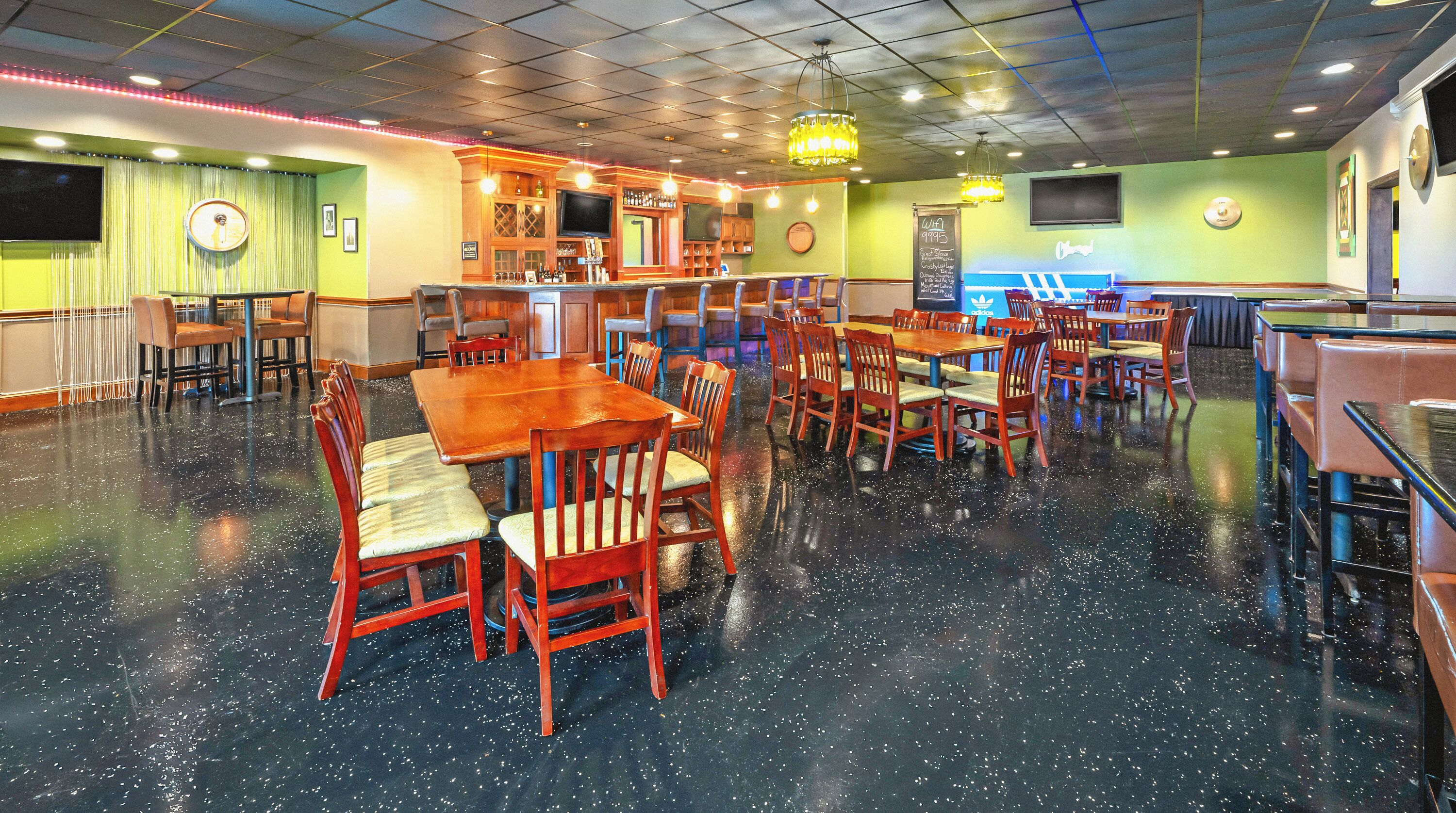 A restaurant with multiple tables and chairs, a bar area, and a chalkboard menu.