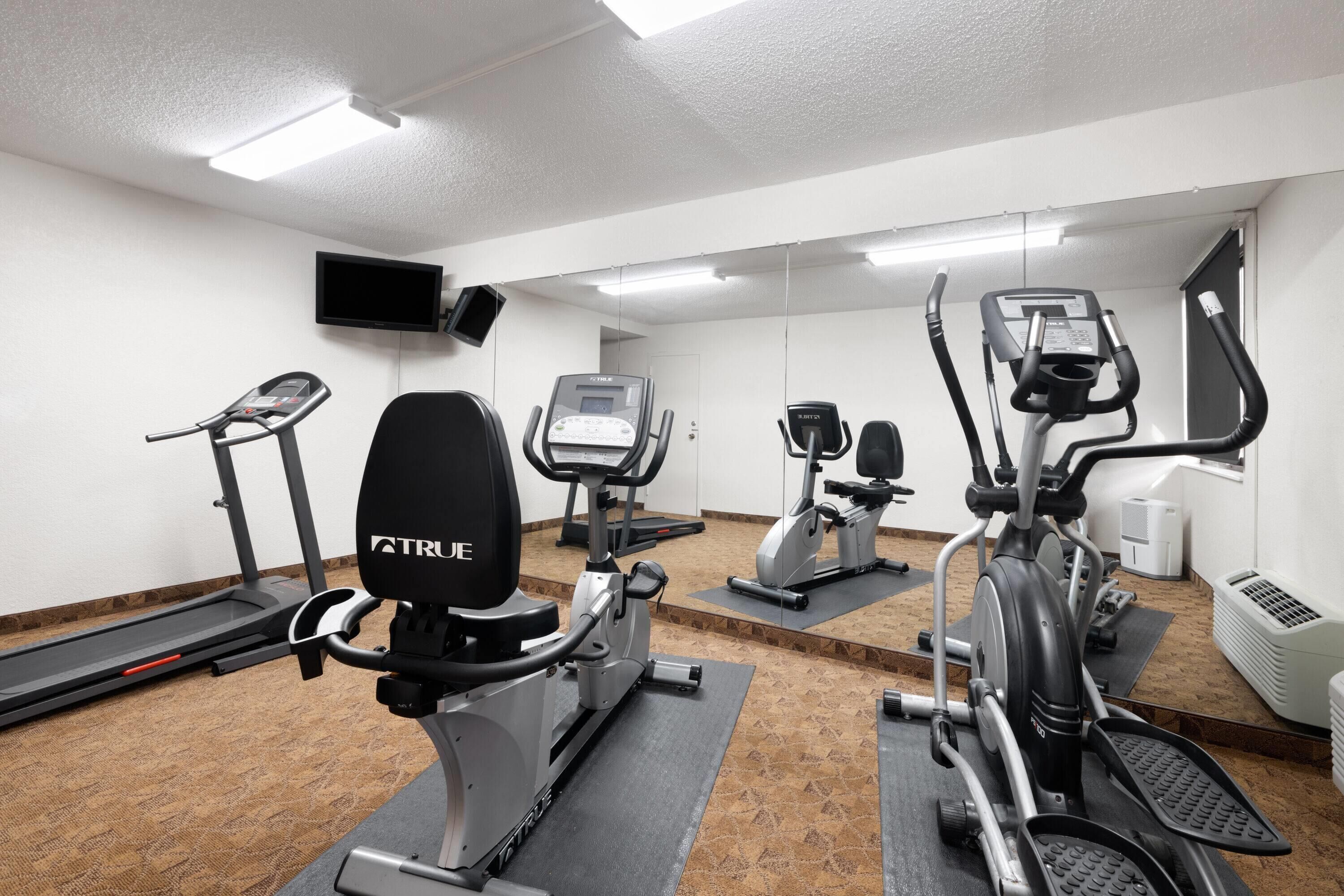 A gym with treadmills, ellipticals, and a stationary bike, equipped with mirrors and a TV.