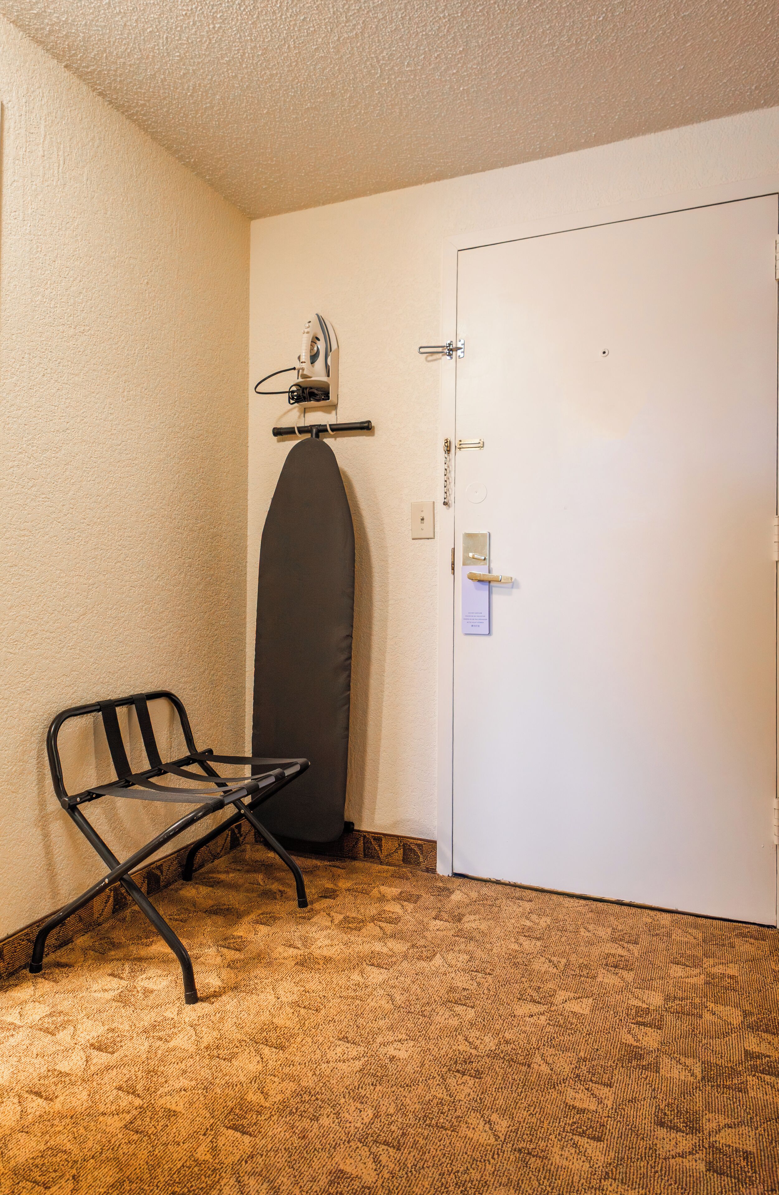 Una habitación con una puerta blanca, una tabla de planchar negra y una silla pequeña.
