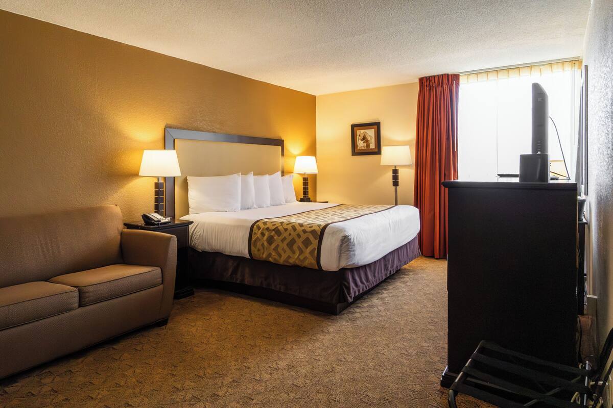 A hotel room with a bed, bedside lamps, a desk, a chair, and a television.