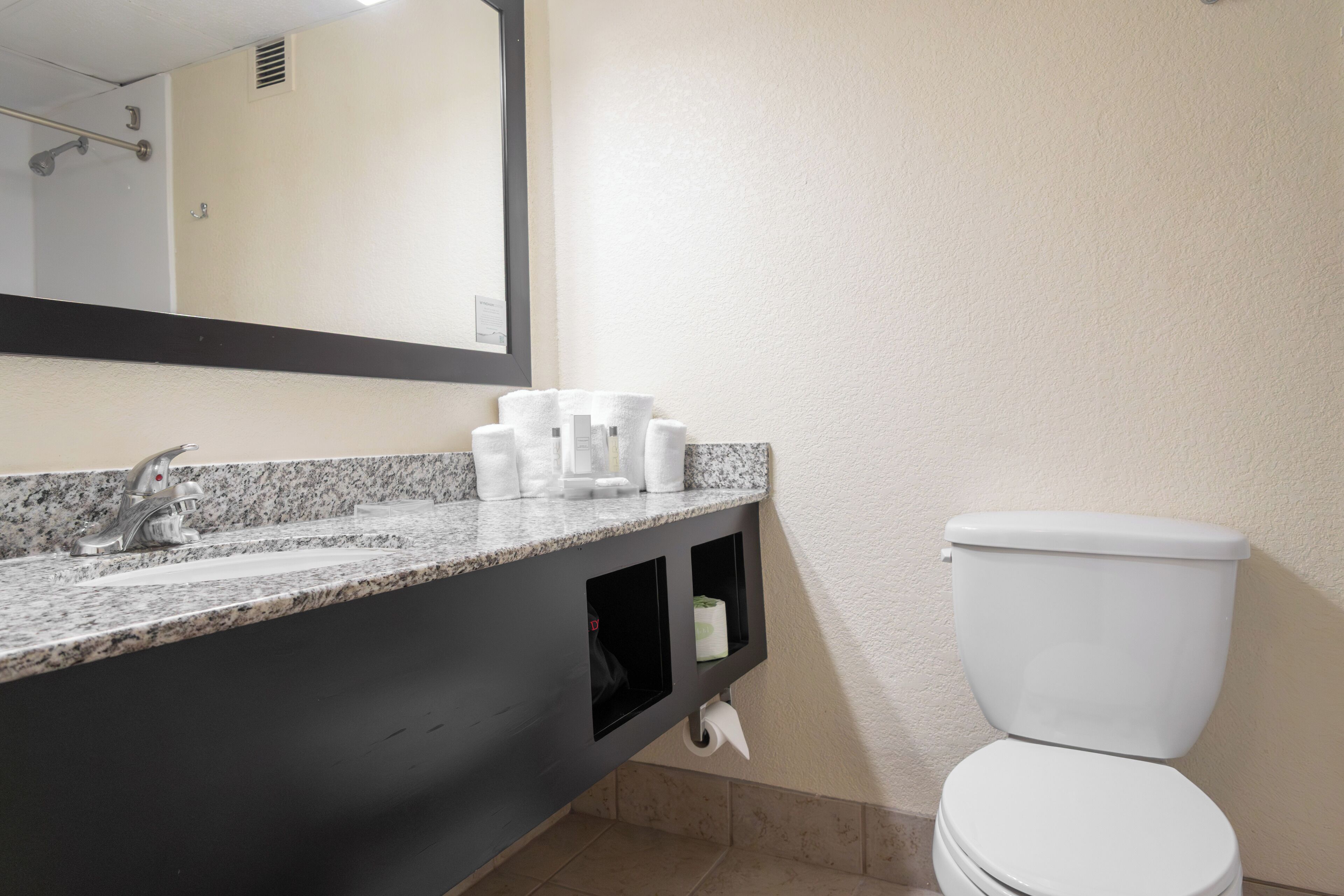 A bathroom with a granite countertop, a white toilet, and a mirror above the sink.