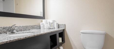 A bathroom with a granite countertop, a white toilet, and a mirror above the sink.
