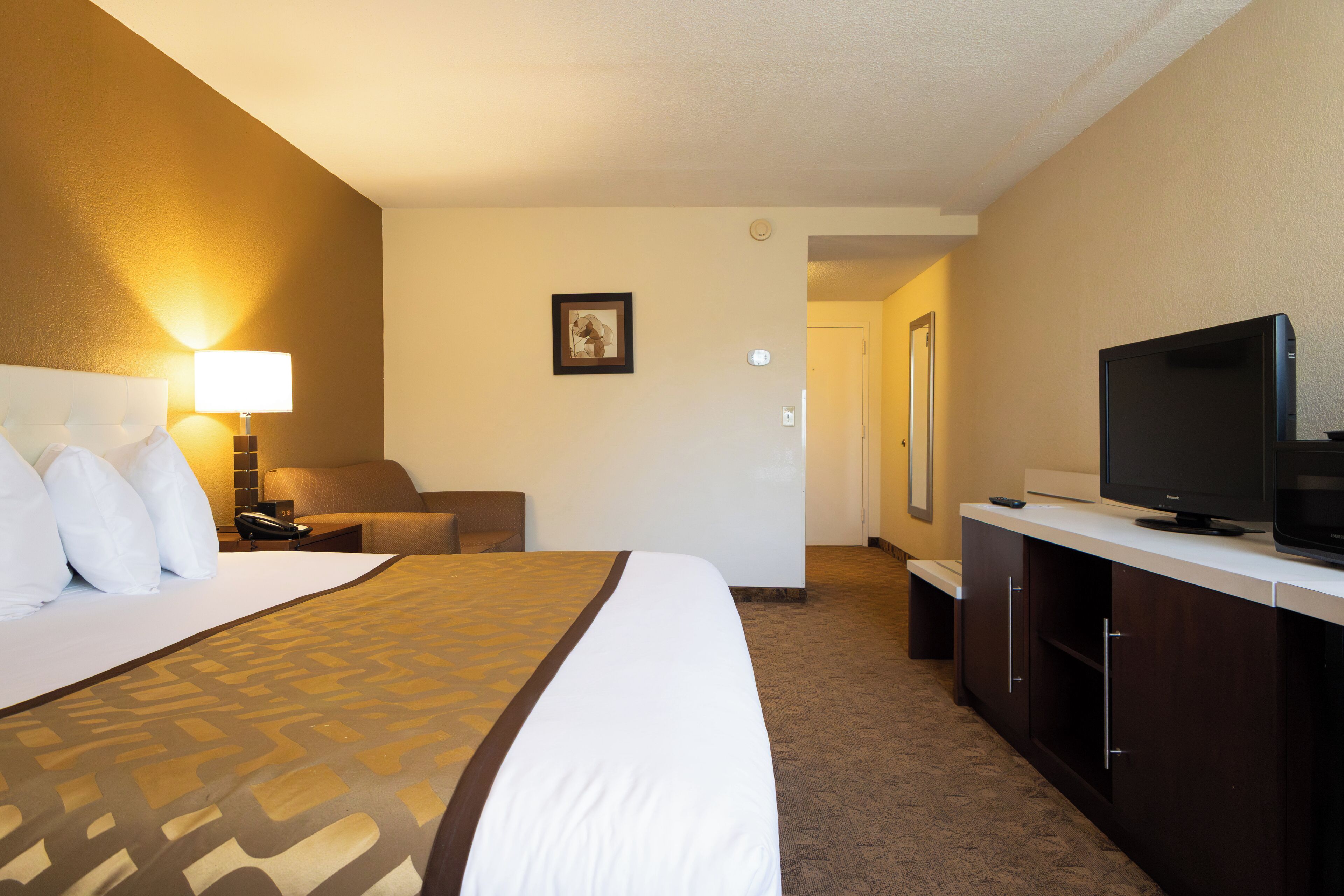 A hotel room with a large bed, a desk with a television, a chair, and a lamp.