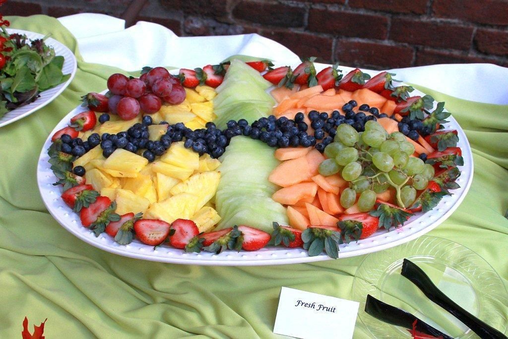 A platter of fresh fruit including strawberries, grapes, pineapple, and carrots, arranged on a white plate.