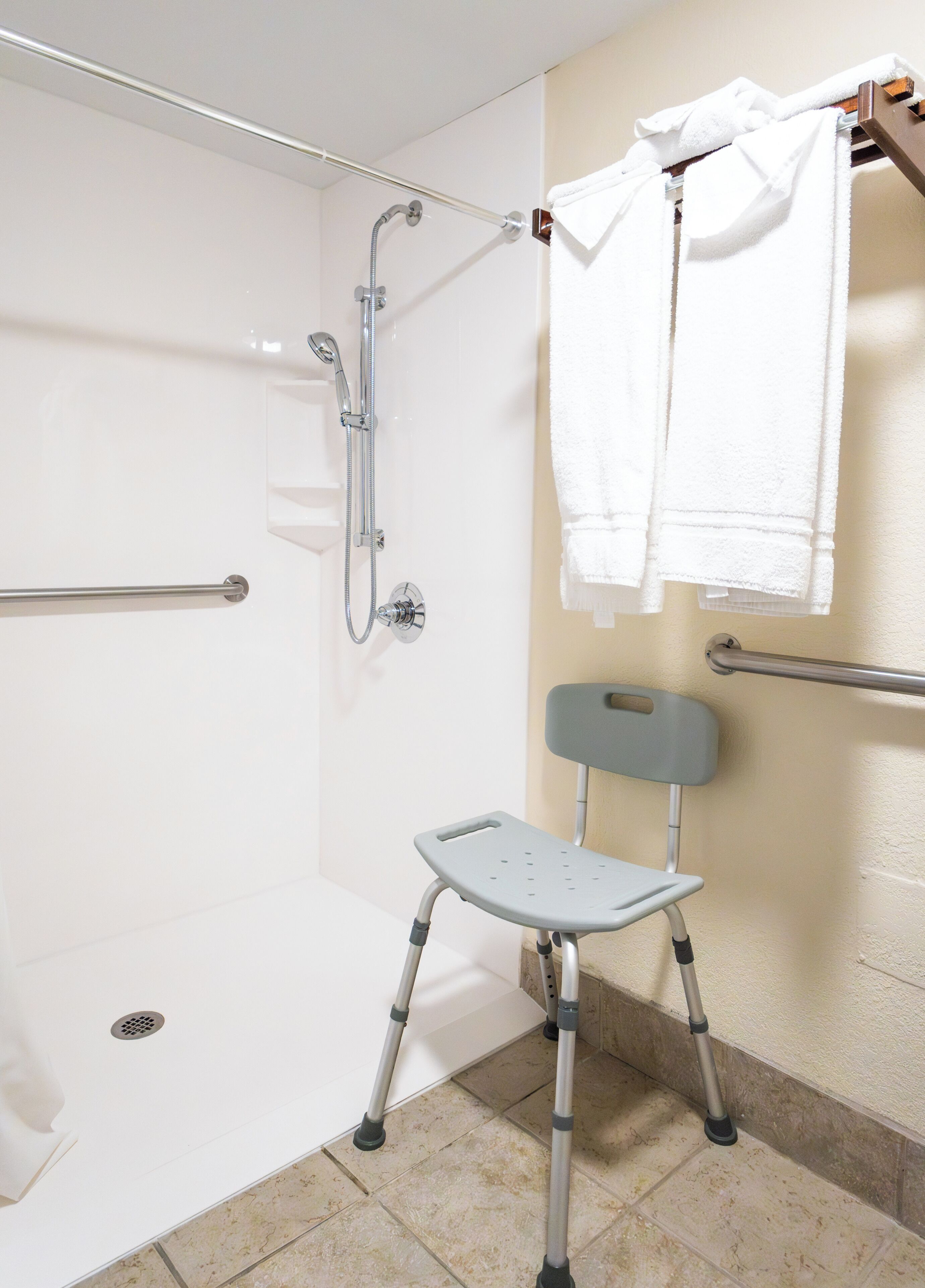 A shower area with a grab bar, a wheelchair-accessible shower seat, and a towel rack with towels.