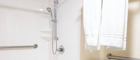 A shower area with a grab bar, a wheelchair-accessible shower seat, and a towel rack with towels.