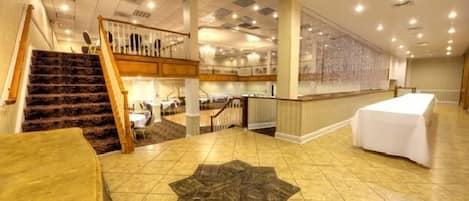 A spacious hotel lobby with a grand staircase, a long reception desk, and a decorative star-shaped rug on the floor.