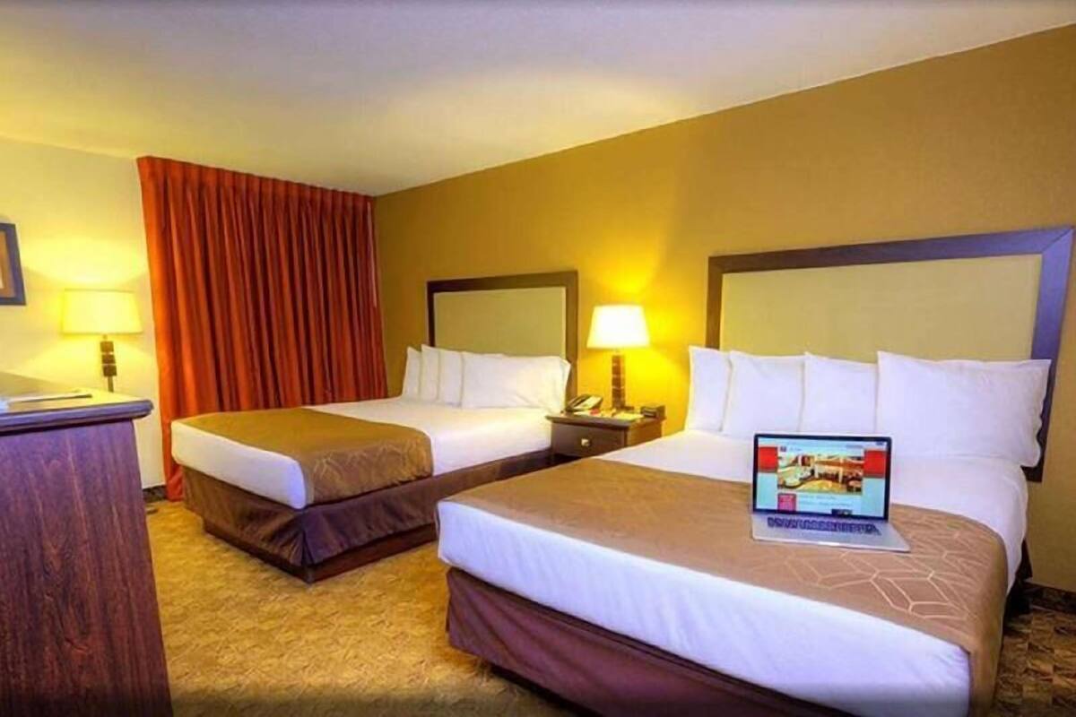 A hotel room with two beds, a desk, a laptop, and a window with curtains.