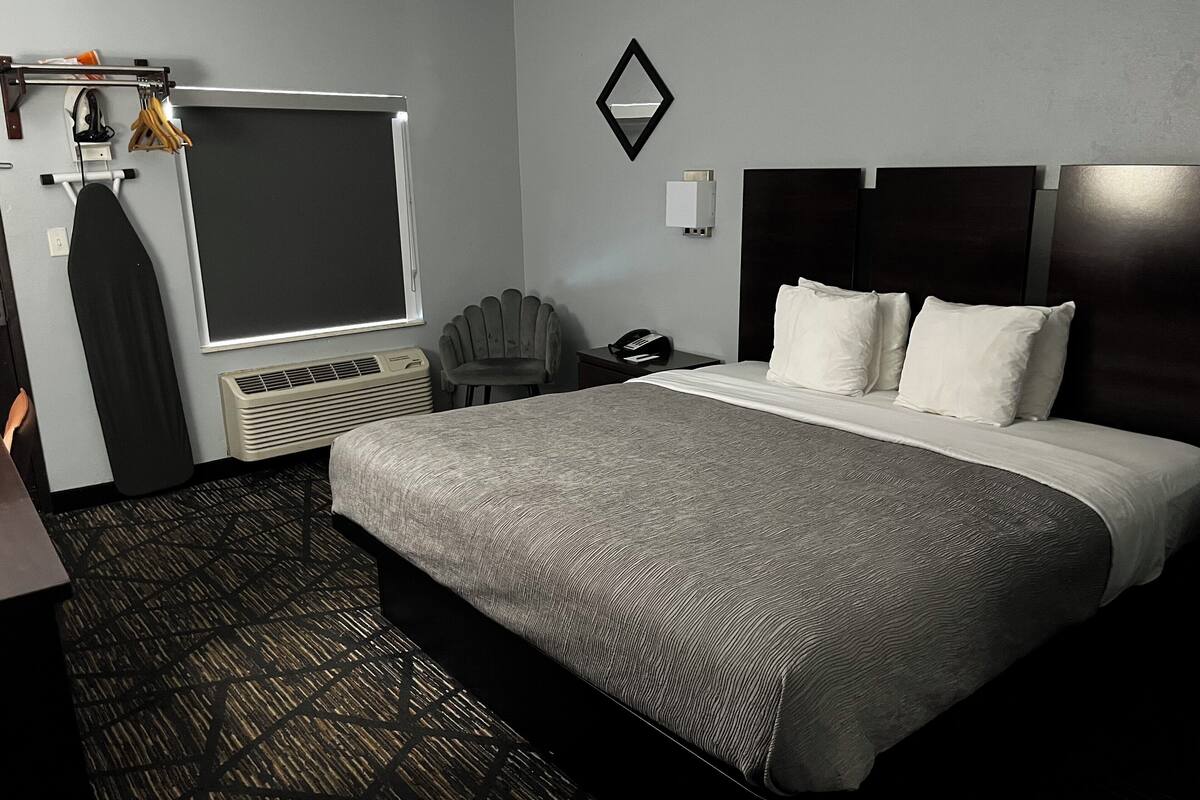 A hotel room with a large bed, a chair, a desk, a telephone, and a window.
