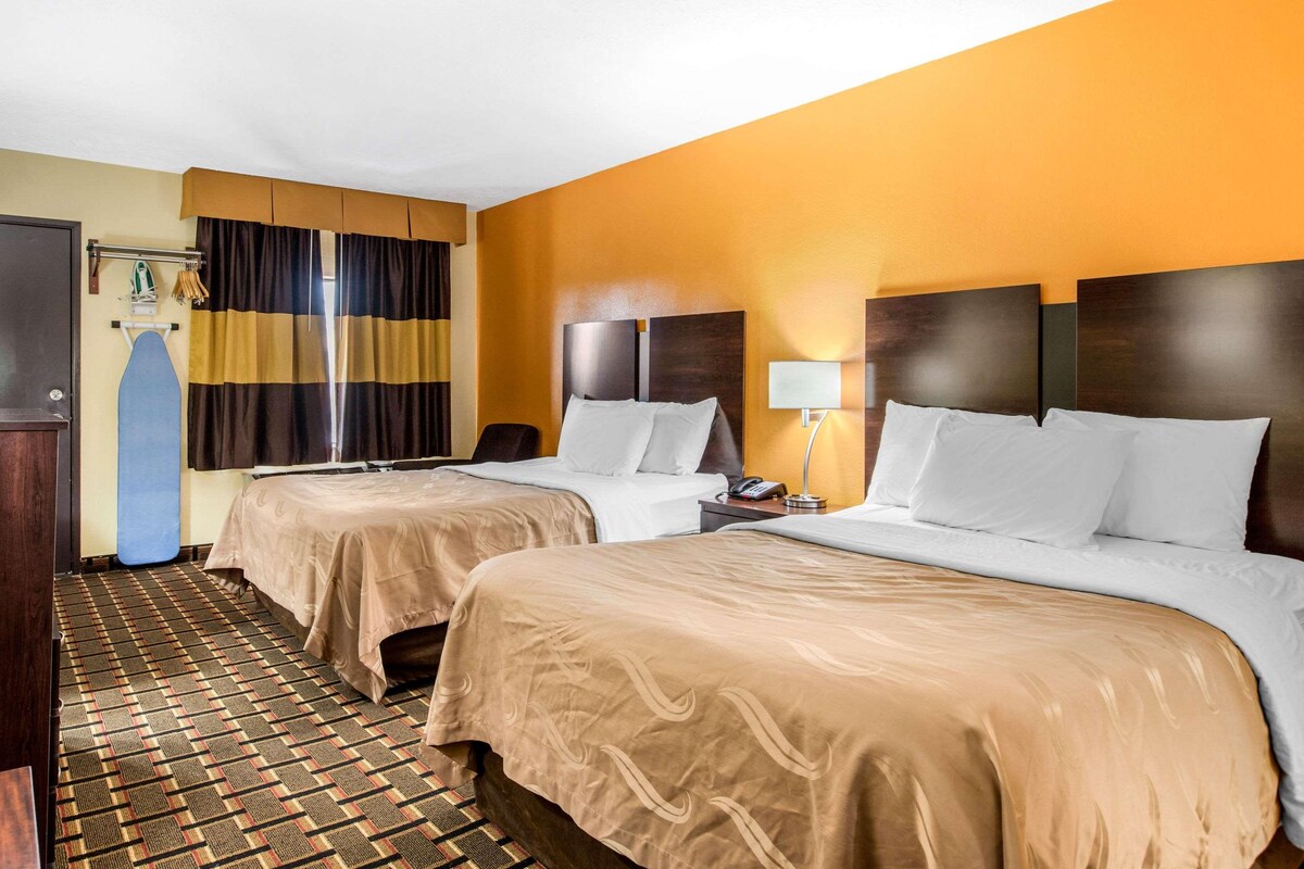 A hotel room with two beds, a desk, a chair, a lamp, and a wardrobe.