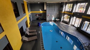 An indoor swimming pool with a blue water feature, surrounded by walls with yellow and grey accents, and a seating area with chairs and a table. - Quality Inn Grand Rapids Near Dowtown (Grand Rapids)