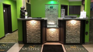 A reception area with two counters, a stone wall, and a green wall with a 'Quality Inn' sign. - Quality Inn Grand Rapids Near Dowtown (Grand Rapids)