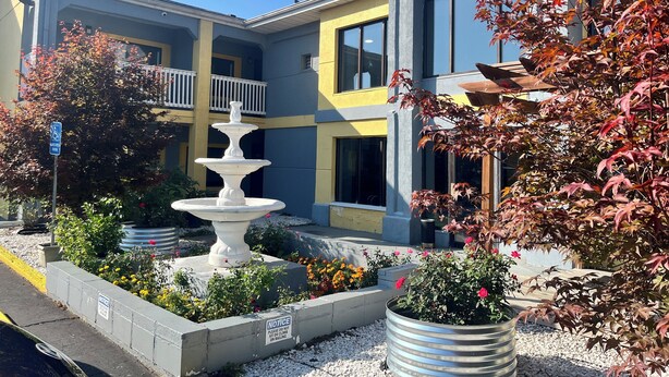 A building with a multi-level balcony, a white fountain, and a garden with various plants and flowers. - Quality Inn Grand Rapids Near Dowtown (Grand Rapids)