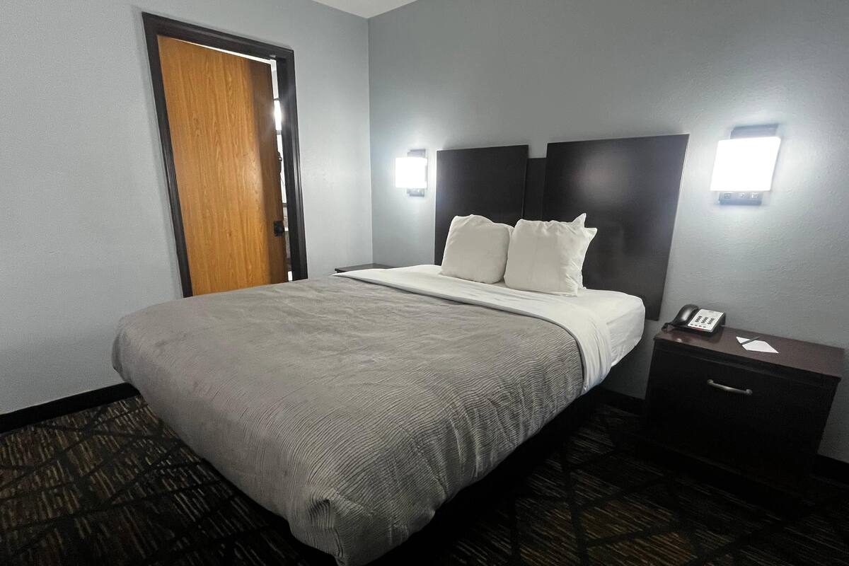 A hotel room with a bed, bedside tables, a telephone, and a door.