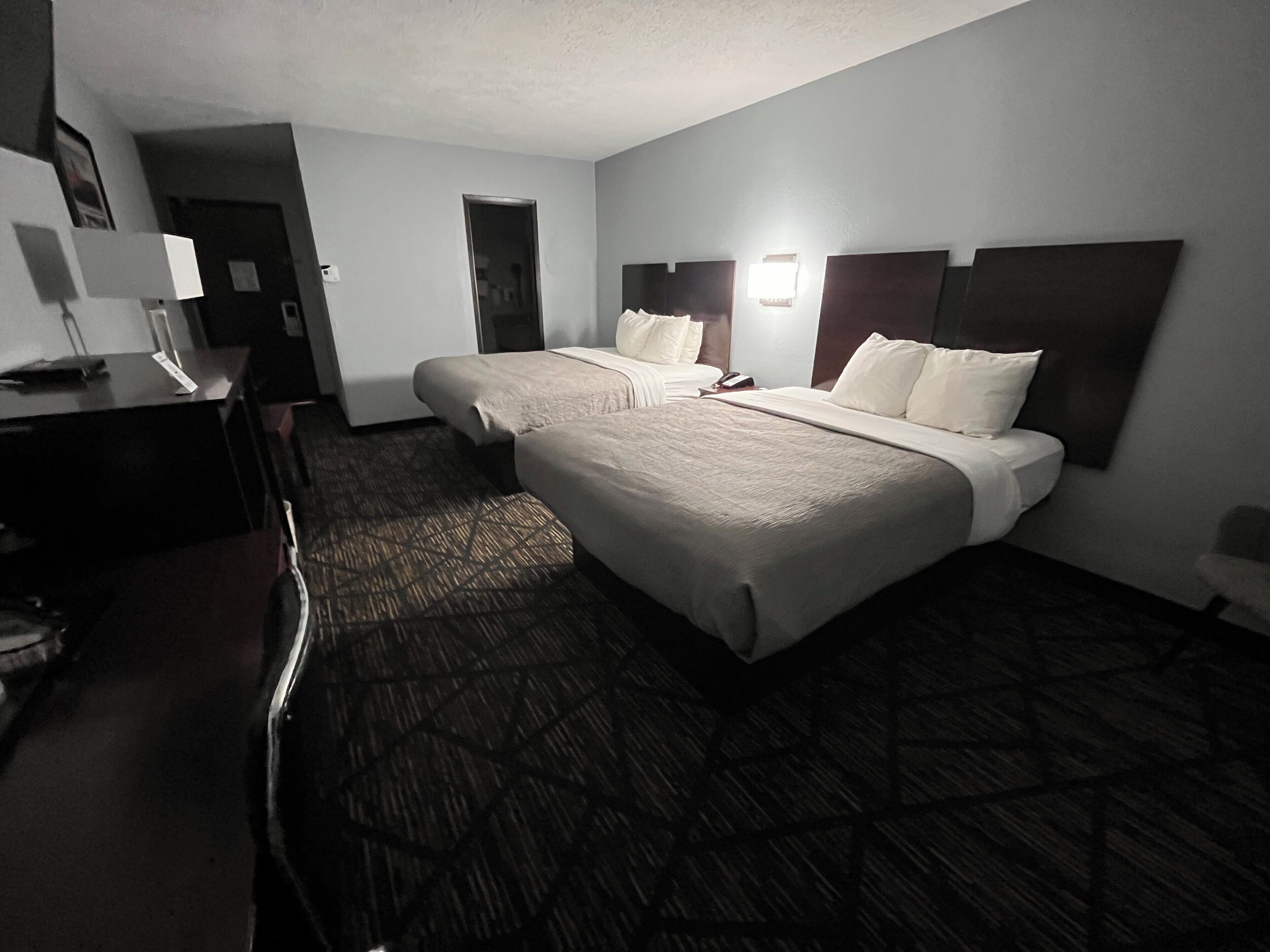 A hotel room with two beds, a desk, and a lamp.