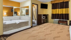 A hotel room with a large bed, a bathroom with a bathtub, a television, and a mirror. - Quality Inn Grand Rapids Near Dowtown (Grand Rapids)
