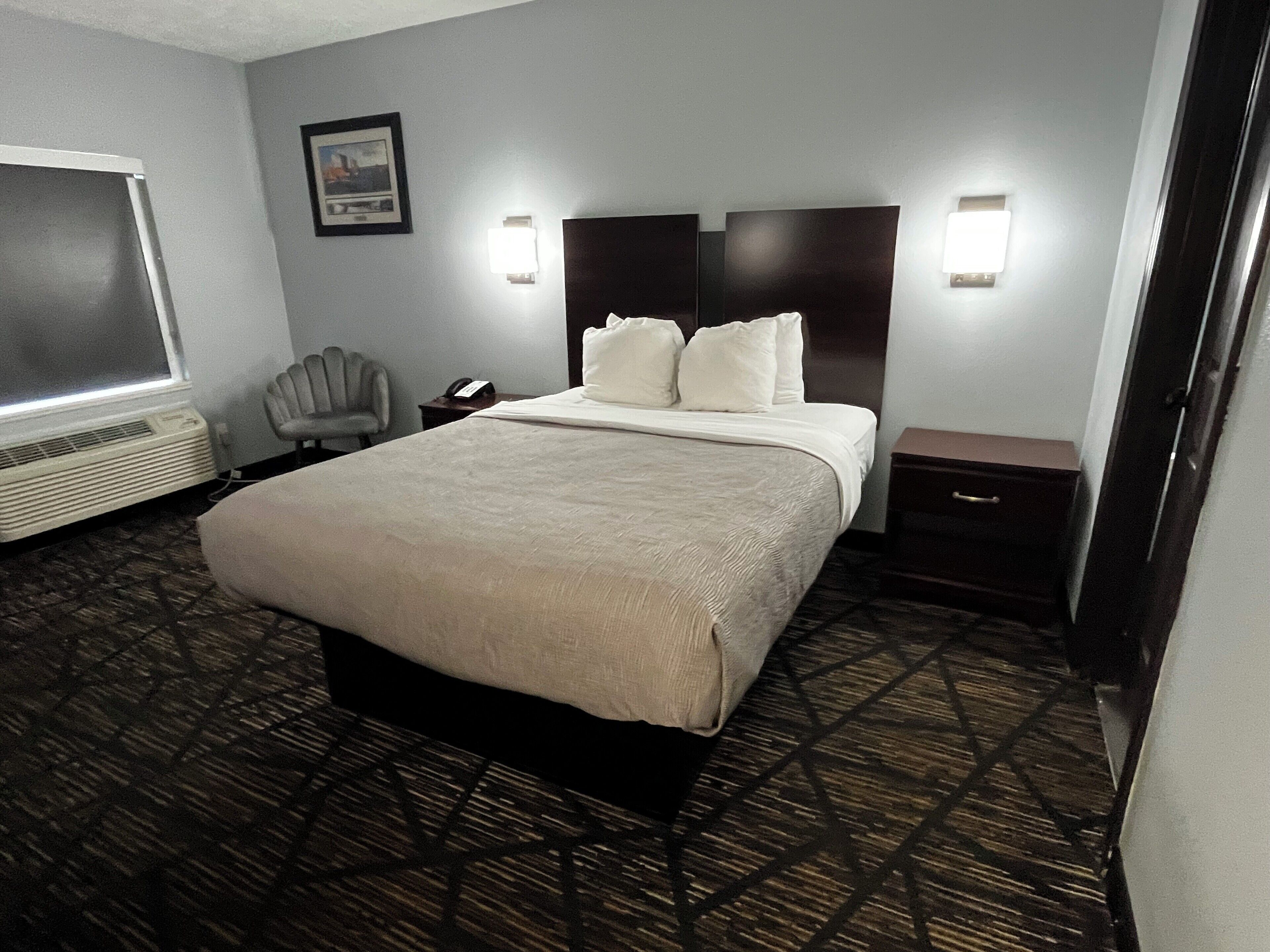Una habitación de hotel con una cama grande, mesitas de noche, una silla, un escritorio y un calentador.