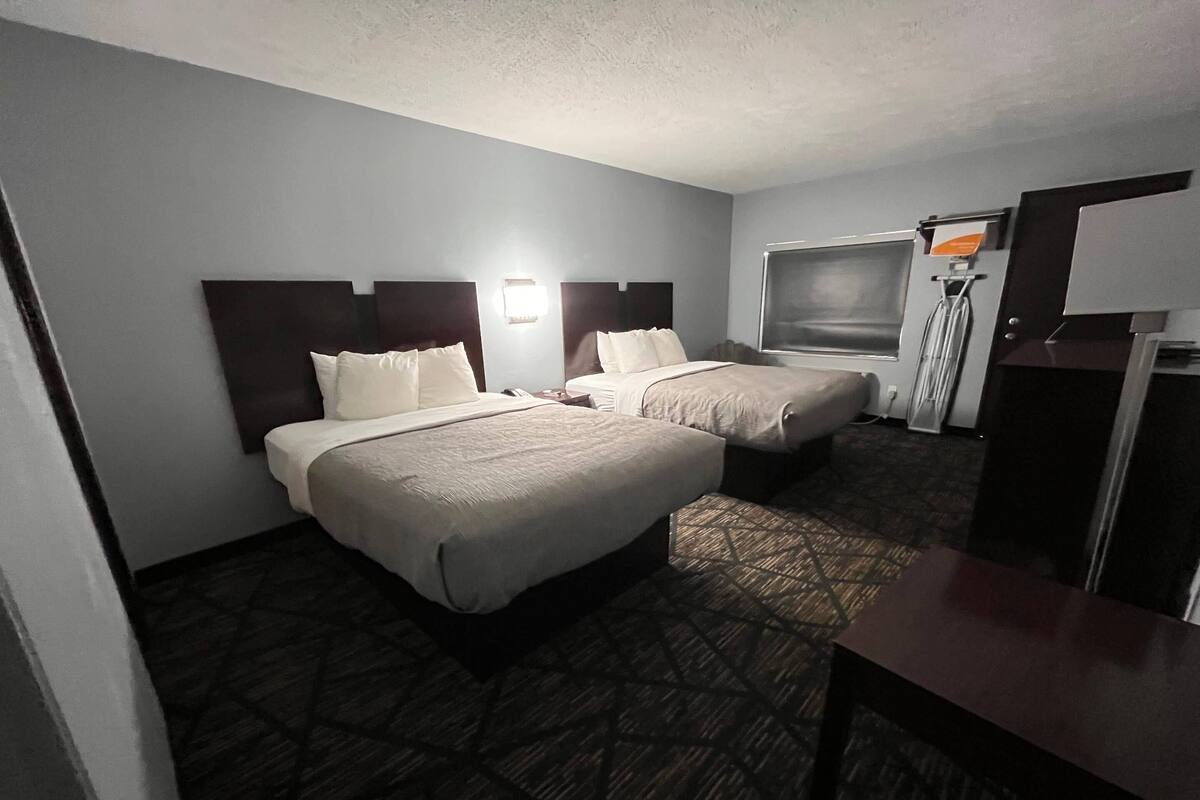 A hotel room with two beds, a TV, a refrigerator, and a desk.