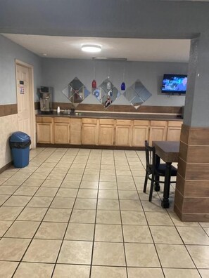 A kitchen area with a tiled floor, wooden cabinets, a coffee machine, and a television mounted on the wall.