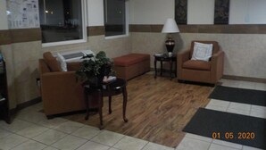 A living room with a brown sofa, a small table with a lamp, and a potted plant. - Motel 6 Hurricane, WV (Hurricane)