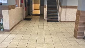 Vestíbulo de hotel con un mostrador de recepción, una escalera y un tapete negro con el logo del número seis.