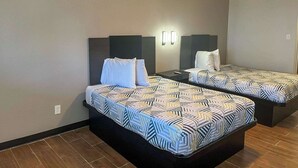 A hotel room with two beds, each with a patterned bedspread and headboards. There are wall-mounted light fixtures and a ceiling light. - Motel 6 Hurricane, WV (Hurricane)