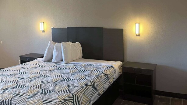 A hotel room with a large bed, two bedside tables, and two wall-mounted lights. - Motel 6 Hurricane, WV (Hurricane)