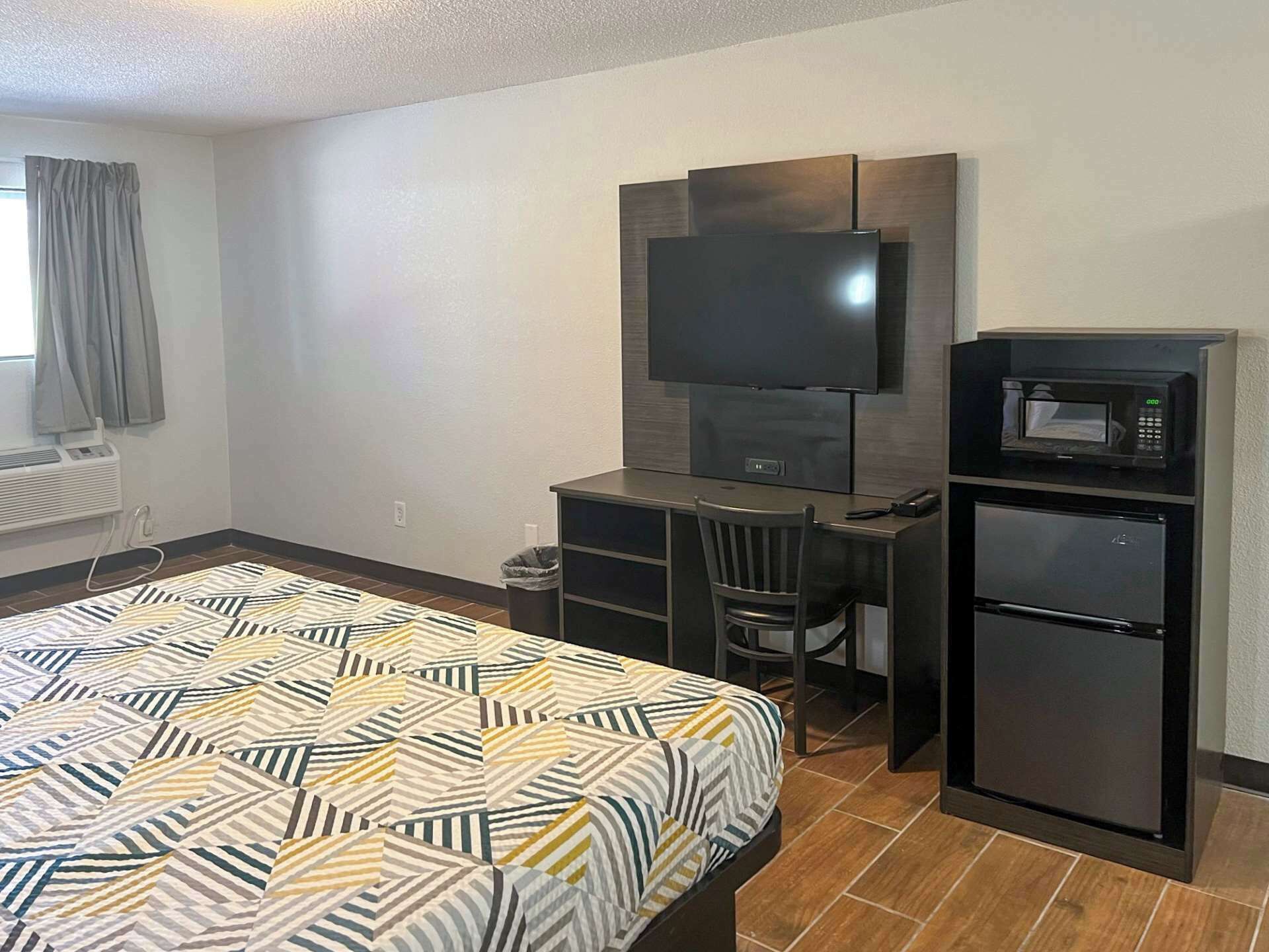 A hotel room with a bed, a desk, a television, a microwave, and a refrigerator.