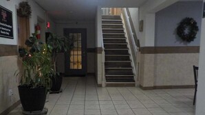 A hotel lobby with a staircase, potted plants, a fire extinguisher, and a sign indicating breakfast for guests only.