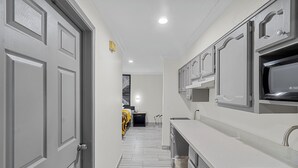 Un pasillo estrecho con una zona de cocina que incluye armarios blancos y un lavamanos de acero inoxidable.