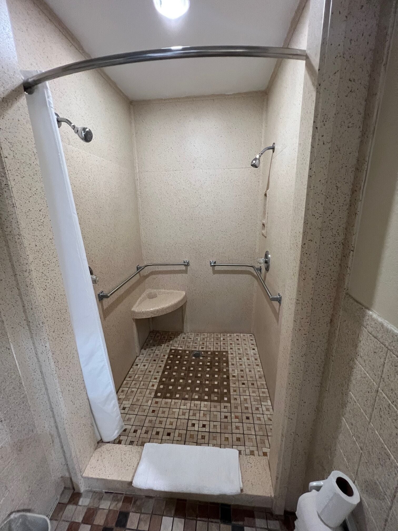 A small, enclosed shower stall with a white sink, grab bars, and a tiled floor.