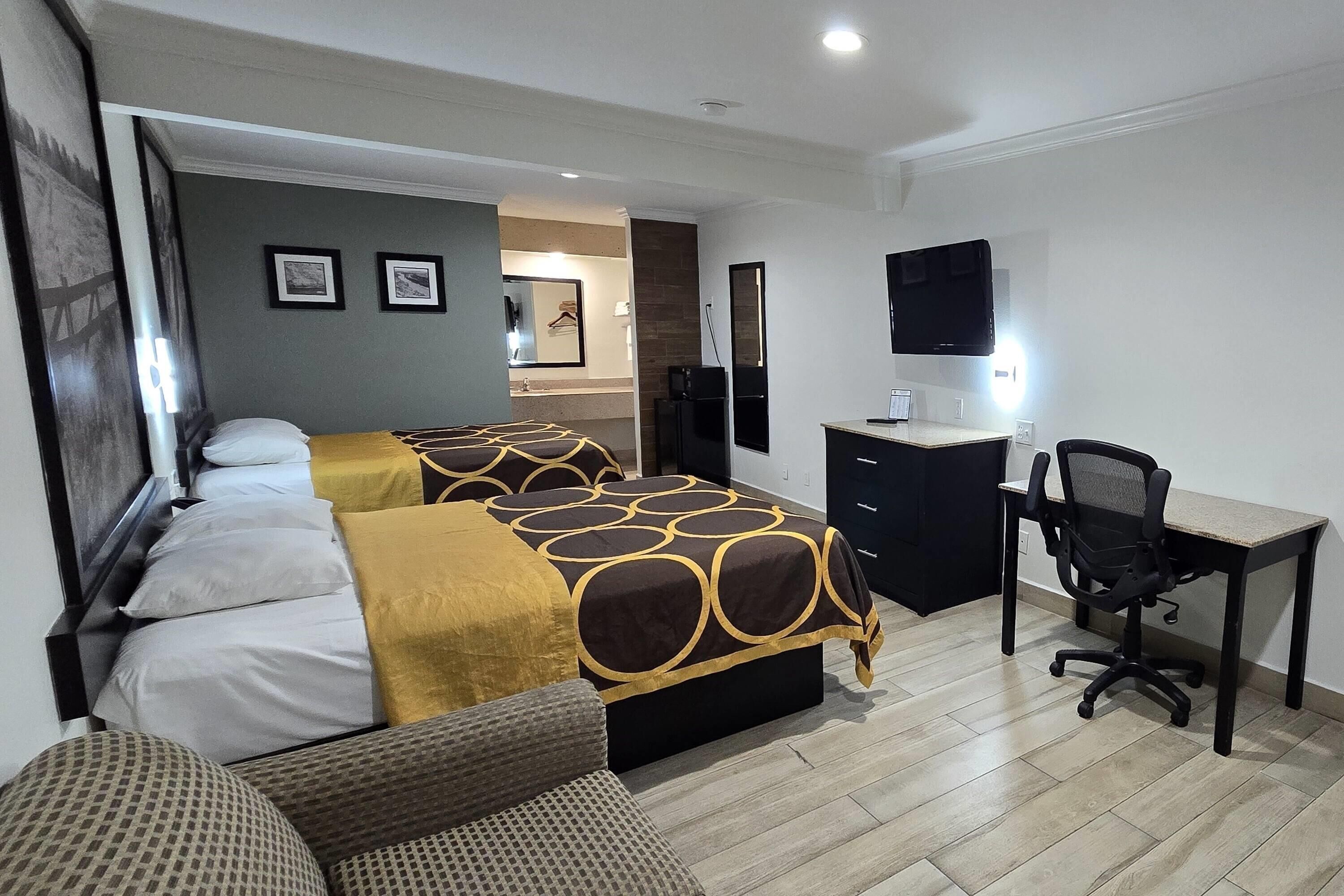 A hotel room with two beds, a desk, a chair, and a TV.
