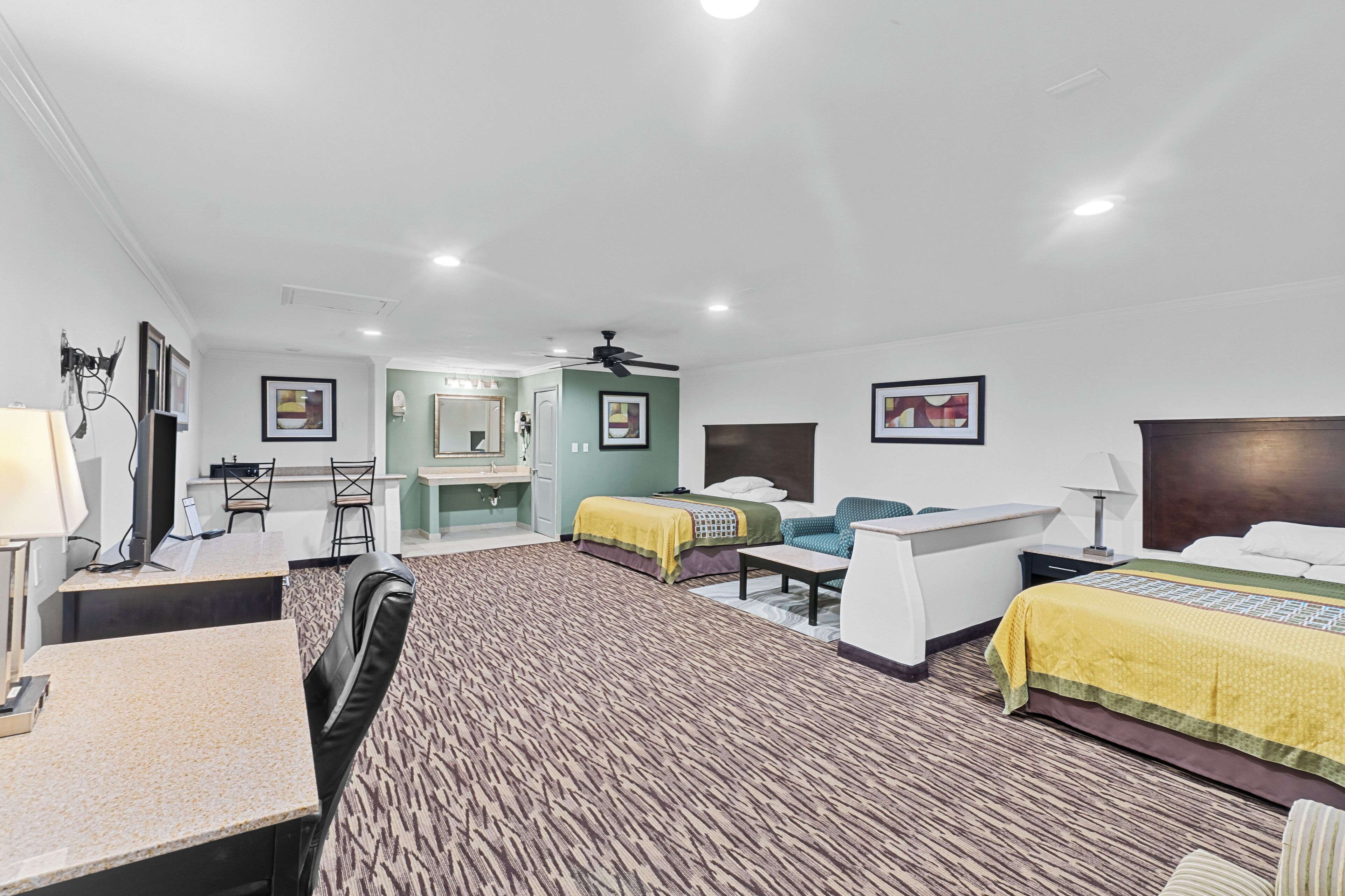 A hotel room with two beds, a desk, a chair, a mirror, and a ceiling fan.
