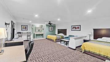A hotel room with two beds, a desk, a chair, a mirror, and a ceiling fan.