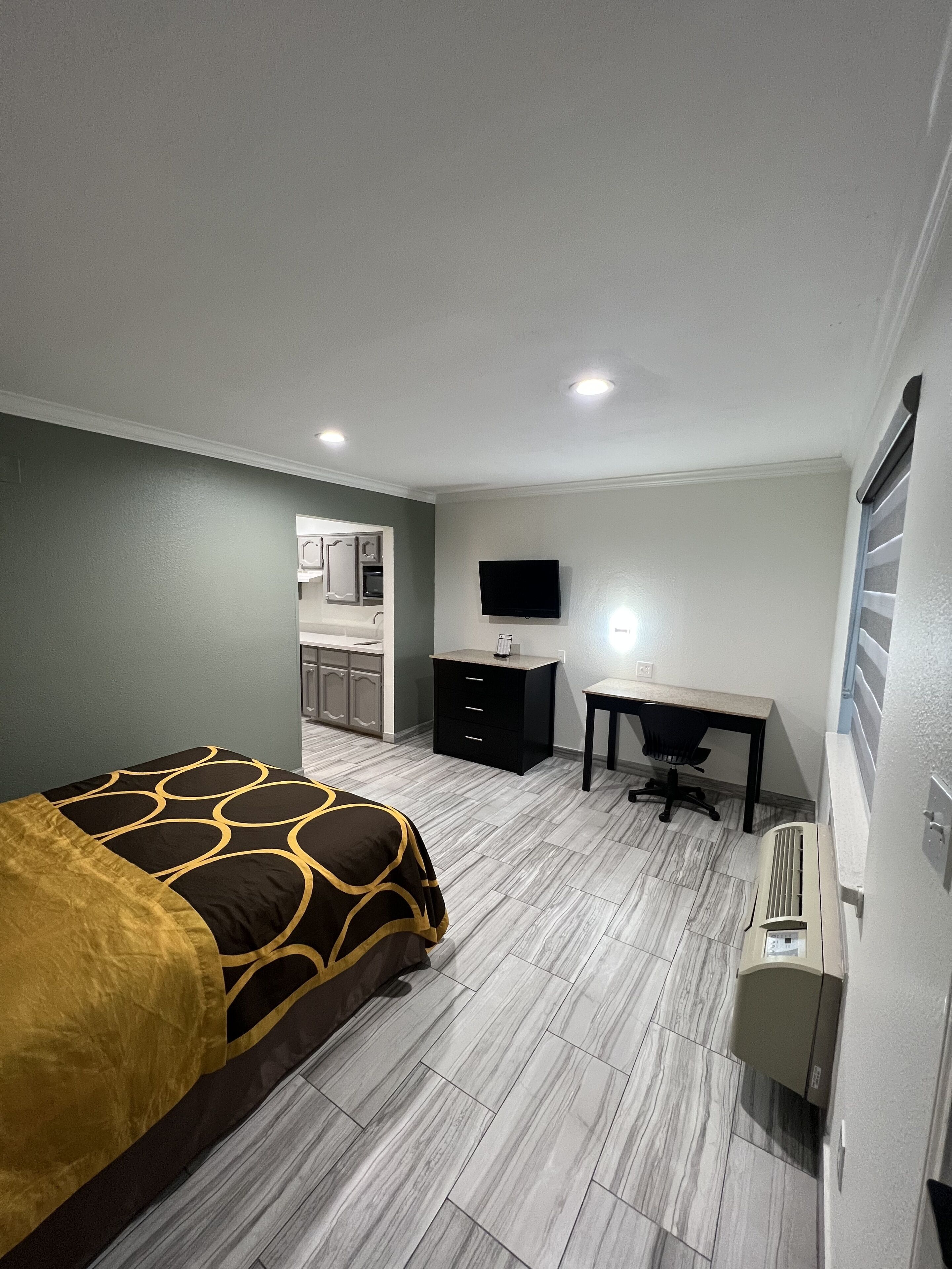 Una habitación de hotel con cama, escritorio, televisor y kitchenette.