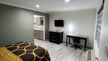 Una habitación de hotel con cama, escritorio, televisor y kitchenette.