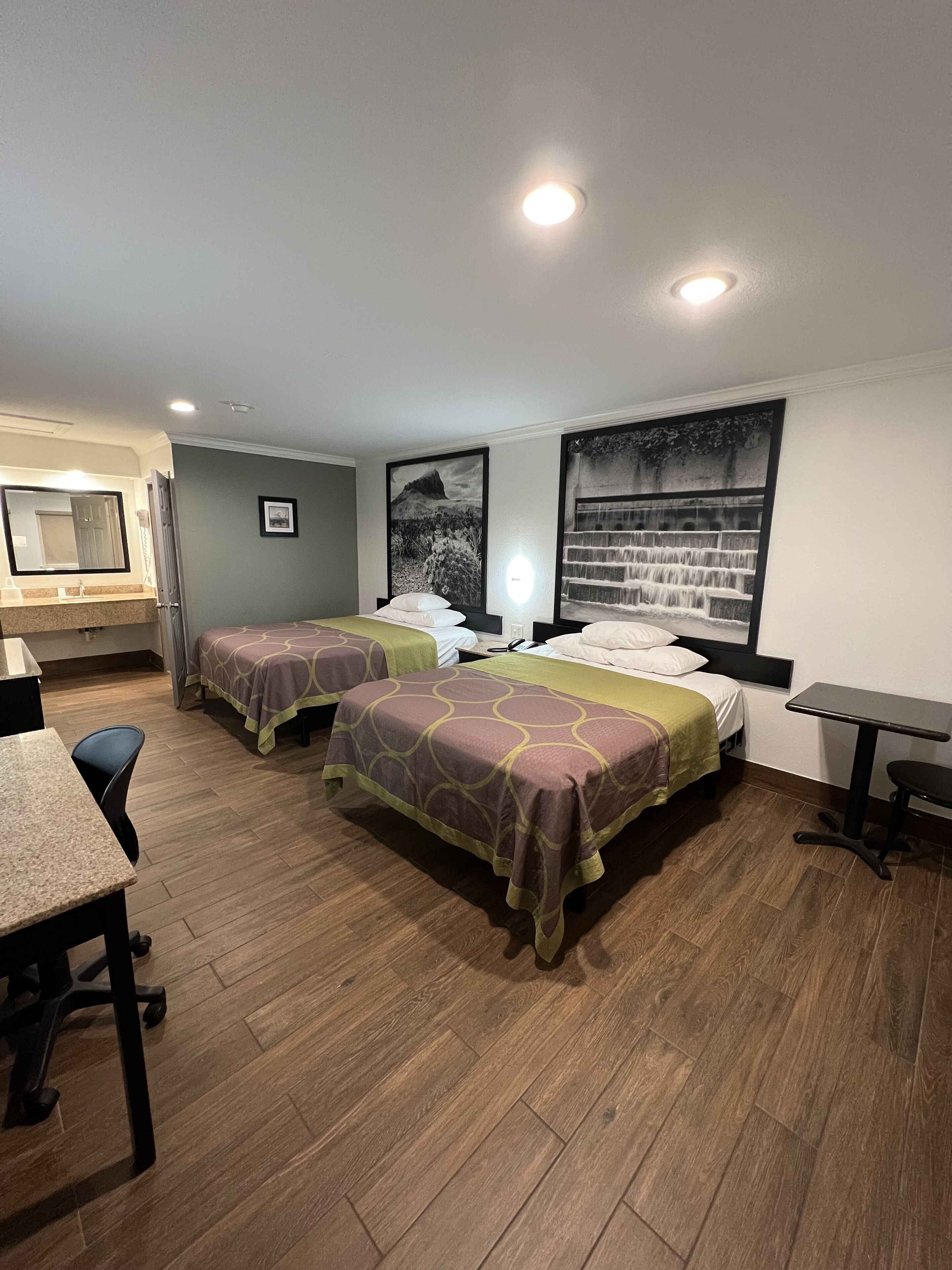 A hotel room with two beds, a desk, a chair, a bathroom with a mirror, and a large window with a waterfall view.