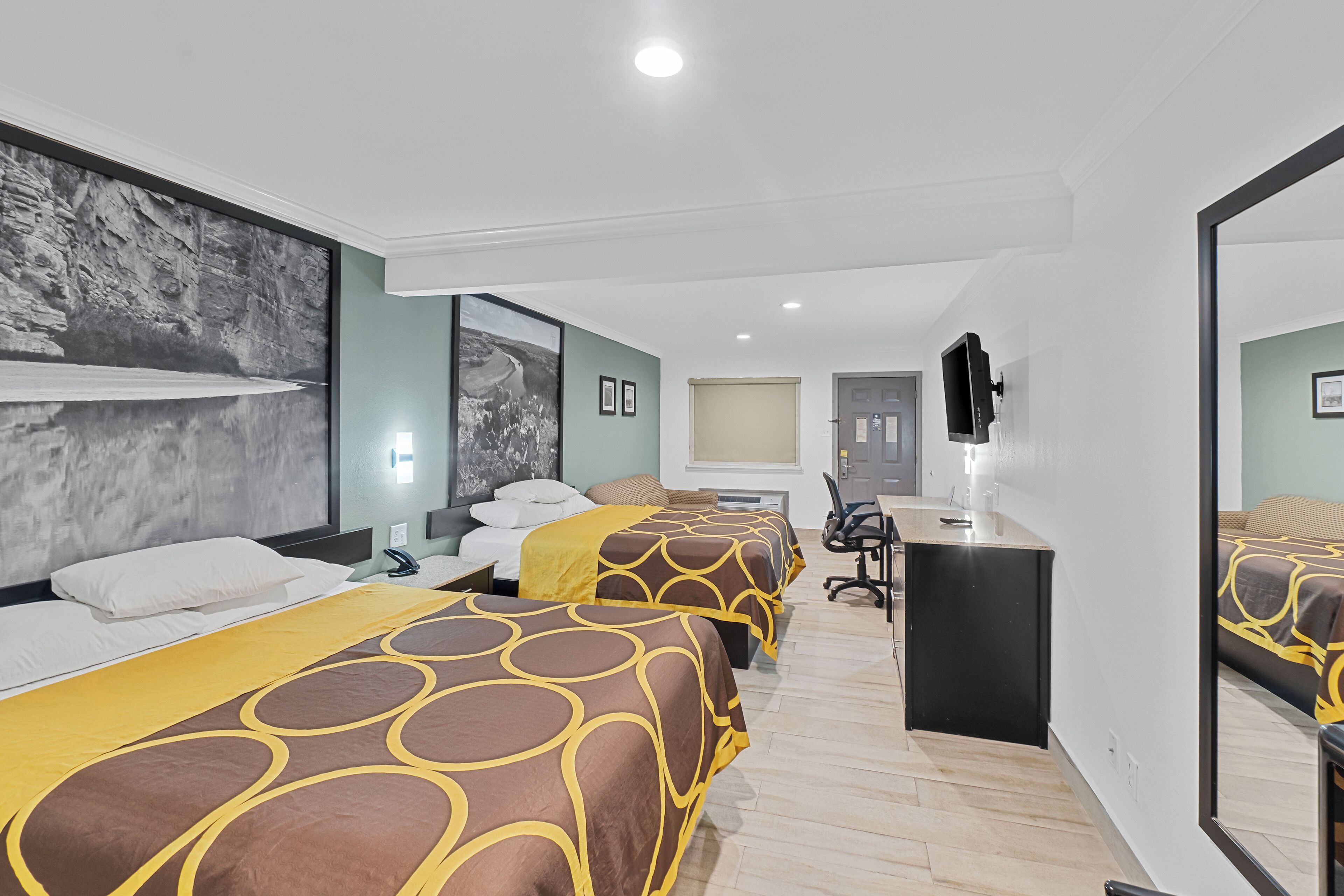 A hotel room with two beds, a desk, and a large mirror.