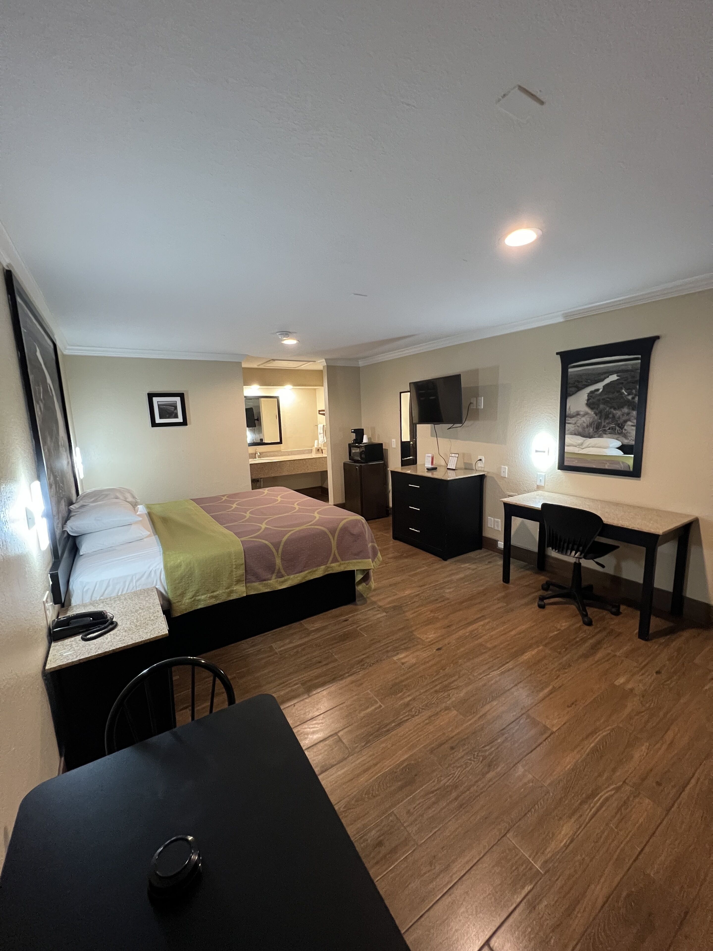 A bedroom with a bed, a desk, a chair, a television, and a picture on the wall.