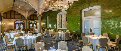 Un salón de banquetes con mesas redondas dispuestas para comer, una araña y paredes con azulejos verdes.