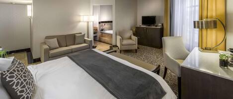 Een hotelkamer met een groot bed, een bank, een bureau, een televisie en een badkamer die door een open deur zichtbaar is.