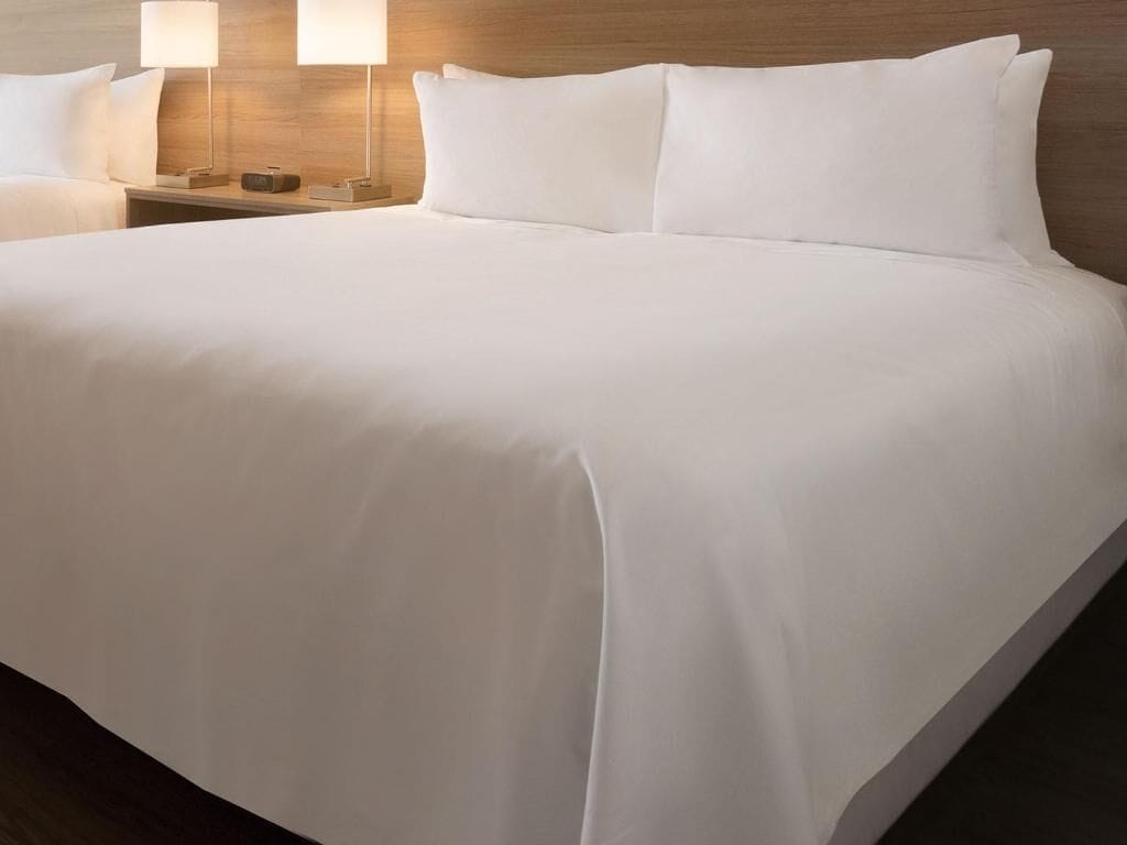 A neatly made bed with white linens, two bedside lamps, and a wooden headboard.