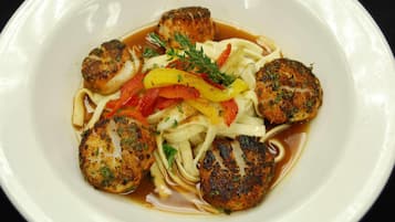 A plate of food with seared scallops, noodles, and sliced bell peppers.