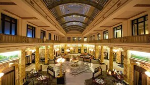 Un vaste hall d’hôtel, doté d’un plafond haut, de colonnes richement décorées et d’une fontaine centrale.