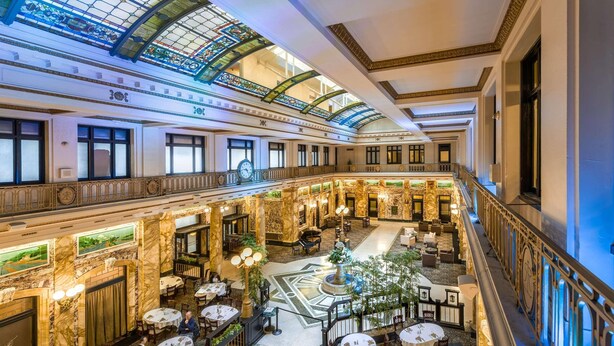 Un hall d’hôtel spacieux avec un patio central, plusieurs espaces de restauration et un grand escalier.