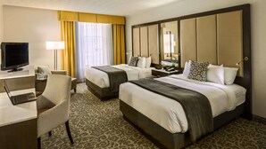 Une chambre d’hôtel avec deux lits, un bureau avec un ordinateur portable, une télévision et un grand miroir.